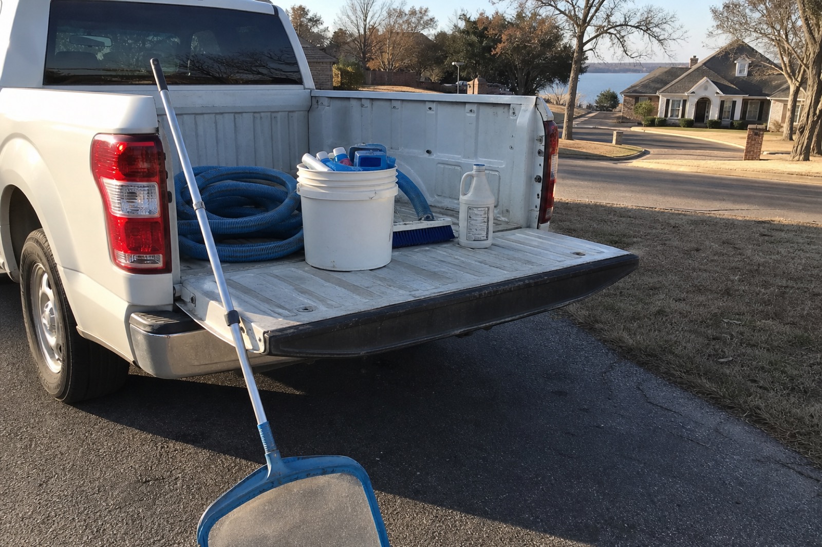 Service truck tailgate on a residential Fort Worth lakeside driveway with telescoping pole, bucket, hoses, and test reagents