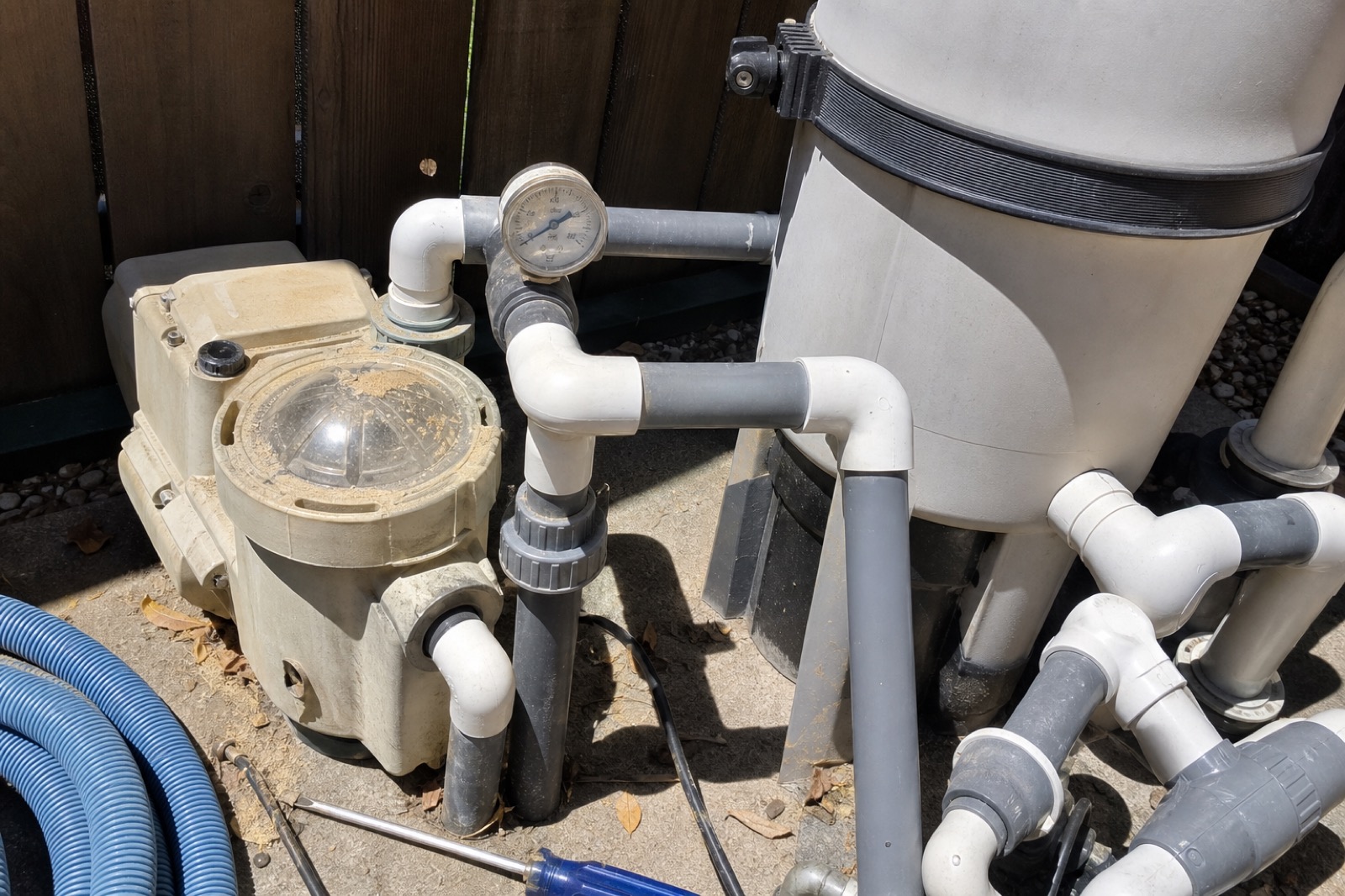 Closeup of a variable-speed pool pump and cartridge filter housing with PVC plumbing and a pressure gauge